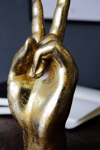 detail image of Gold Peace Hand Ornament on wooden table with open book in background