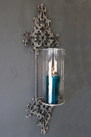 lifestyle image of metal filigran candle wall sconce with blue candle inside on grey wall background